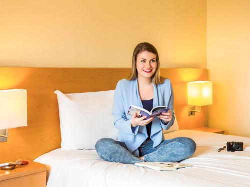 a woman sitting on a bed reading a book at ibis Deira Creekside Dubai in Dubai