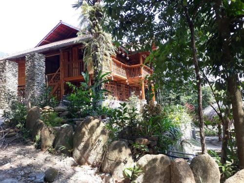 a wooden house with trees and rocks in front of it at Ha Giang Faithien Homestay in Ha Giang