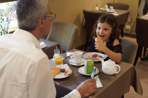 a man and a little girl sitting at a table eating food at Cit'Hotel La Résidence in Nancy
