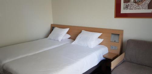 two twin beds in a room with a chair at Novotel Narbonne Sud A9/A61 in Narbonne