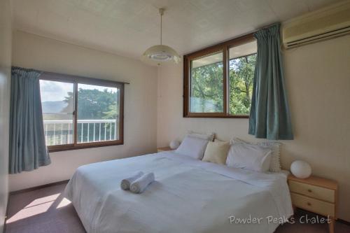 a bedroom with a large white bed with windows at Powder Peaks Chalet in Akakura