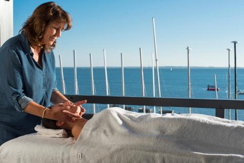 a woman sitting on a bed looking at the ocean at L'Anderenis Boutique Hôtel in Andernos-les-Bains