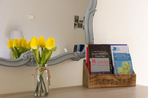 a vase with yellow flowers and a mirror and books at Millbrae Lodges in Belfast