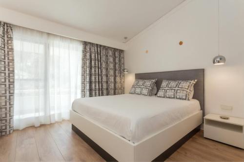a white bedroom with a large bed and a window at Blue&Greens Apartment in Quinta do Lago