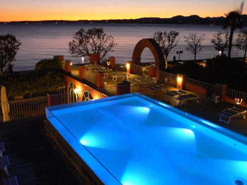 a blue swimming pool with a view of the water at Hotel Alla Riviera in Bardolino