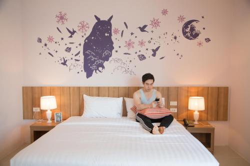 a woman sitting on a bed looking at her cell phone at The Bedroom Ladprao 101 Bangkok - SHA in Bangkok