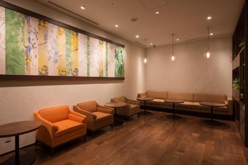 a waiting room with tables and chairs and a large painting at HOTEL FORZA HAKATAEKI CHIKUSHI-GUCHI Ⅰ in Fukuoka
