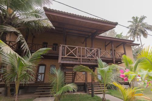 a house with a balcony and some palm trees at Hotel Coucoue Lodge in Assinie