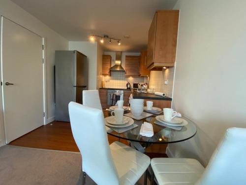 cocina con mesa de cristal y sillas blancas en Central Milton Keynes hub one bedroom secured apartment, en Milton Keynes