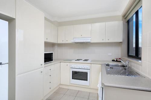 a white kitchen with white cabinets and a sink at Wollongong Serviced Apartments in Wollongong