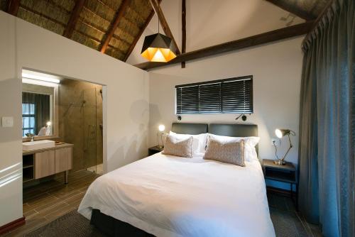a bedroom with a white bed and a bathroom at Buckler's Africa Lodge Kruger Park in Komatipoort