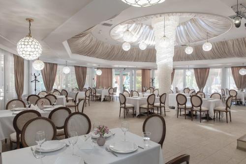 una sala da pranzo con tavoli e sedie bianchi e lampadari a braccio di Jardin Park Hotel a Rostov sul Don