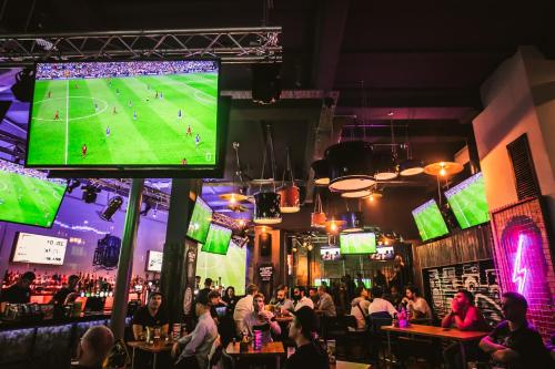 een groep mensen zit in een bar met een grote tv bij St Christopher's Hammersmith in Londen