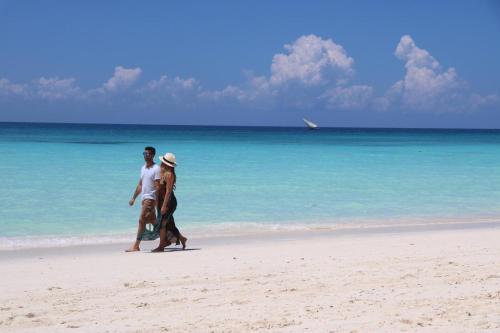 a man and a woman walking on the beach at Badolina Bungalows in Nungwi