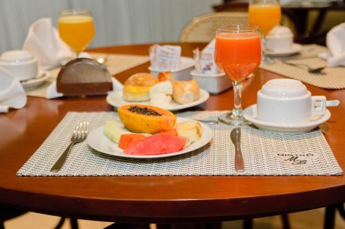 une table avec des assiettes de nourriture et deux verres de jus d'orange dans l'établissement Mont Blanc Apart Hotel Nova Iguaçu, à Nova Iguaçu