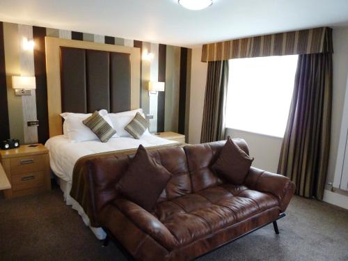 a hotel room with a bed and a leather couch at Trivelles Park Hotel in Preston