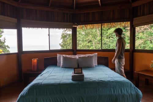a person standing in a bedroom looking out the windows at Hotel Vista de Olas in Santa Teresa Beach
