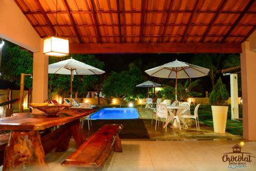 un patio con piscina, mesas y sombrillas en Chocolat Barra Beach, en Maraú