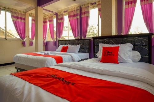 two beds with red pillows in a room with windows at RedDoorz near RSUD Kebumen in Kebumen