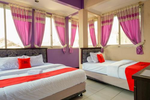 two beds in a room with pink and purple curtains at RedDoorz near RSUD Kebumen in Kebumen