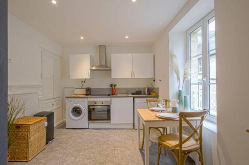 une cuisine avec des armoires blanches et une table avec des chaises dans l'établissement Victoire Duplex atypique cosy - PLEIN CENTRE HISTORIQUE BAYEUX PROCHE RESTAURANTS COMMERCES- LUMINEUX - PARKING GRATUIT A PROXIMITE- proche plages du débarquement, Omaha Beach, à Bayeux