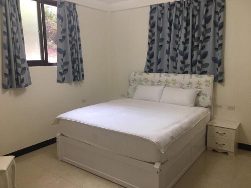 a bedroom with a white bed with blue curtains at Kinmen Huquian 58 in Jinhu