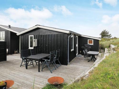 a black cottage with a table and chairs on a deck at 7 person holiday home in L kken in Løkken