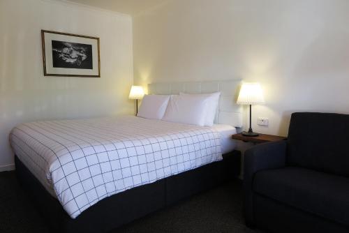 a hotel room with a bed and a chair at Summerhill Motor Inn in Merimbula