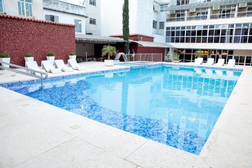 a large swimming pool with white chairs and a building at Ritz Plaza Hotel in Juiz de Fora