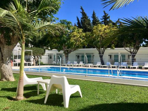a resort with a swimming pool with white chairs and trees at Hostal Las Cumbres in Conil de la Frontera