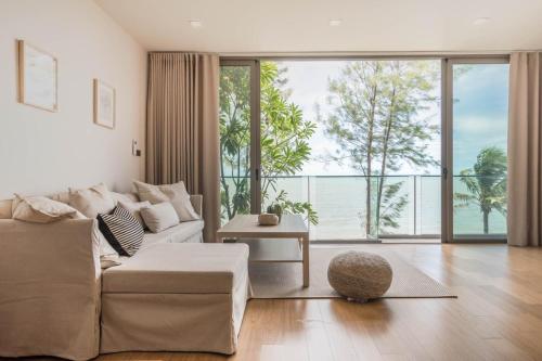 a living room with a white couch and a large window at Sandbox Beachfront Villa 3 in Ban Krathing Lai