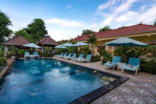 a swimming pool with chairs and umbrellas next to a house at Bali Nusa Cottage in Nusa Lembongan