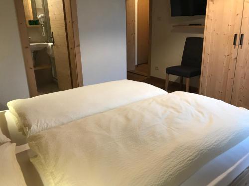 a white bed in a room with a chair at Platzerhof in Monguelfo