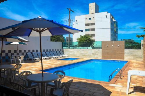 a pool with tables and chairs and an umbrella at Thanharu Praia Hotel in Anchieta