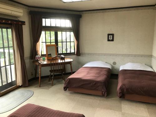 two beds in a room with a desk and windows at Pension Marionette in Hakuba