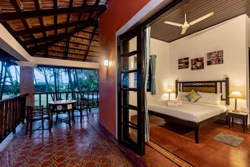 a bedroom with a bed and a balcony with a table at SaffronStays Blue Flag House, a 3-BDR beachfront villa in Hejamady in Mangalore