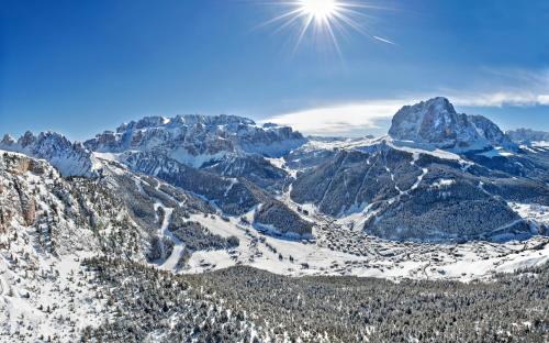 a snow covered mountain range with the sun in the sky at The Oswald Grand Hotel in Selva di Val Gardena