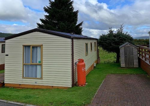 a small white shed with a fire hydrant next to it at 22 Aimie Lodge in Boat of Garten