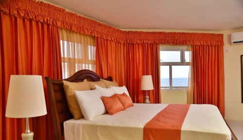 a bedroom with a bed with orange curtains and a window at Hotel Grand A View in Montego Bay