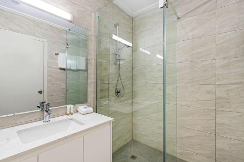 a bathroom with a glass shower and a sink at Knox International Hotel and Apartments in Wantirna