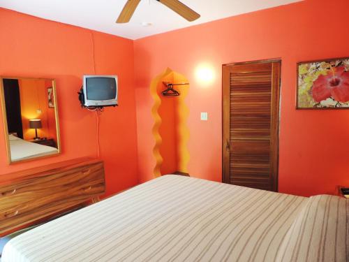 a bedroom with orange walls and a bed and a tv at Sunrise Club Hotel in Negril