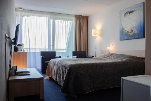 a hotel room with a bed and two chairs and a window at Strandhotel Buren aan Zee in Buren