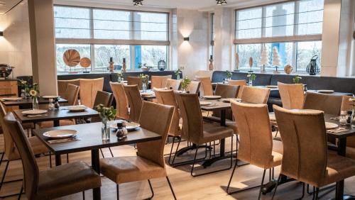 un comedor con mesas, sillas y ventanas en Strandhotel Buren aan Zee en Buren