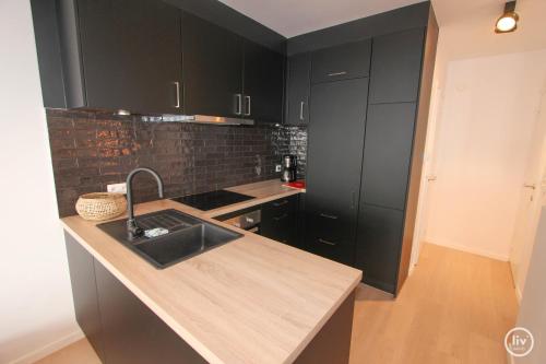 eine Küche mit schwarzen Schränken und einem Waschbecken in der Unterkunft Lily a la mer du Zoute in Knokke-Heist