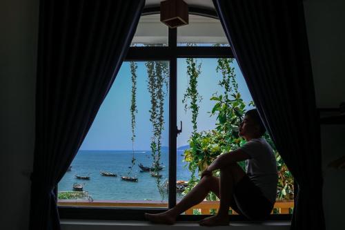 a woman sitting in a window looking out at the ocean at Sunbay Homestay Cu Lao Cham in Tân Hiệp