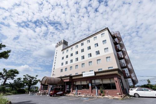 um edifício branco com carros estacionados num parque de estacionamento em Tabist Tsukuba Sky Hotel em Tsukuba