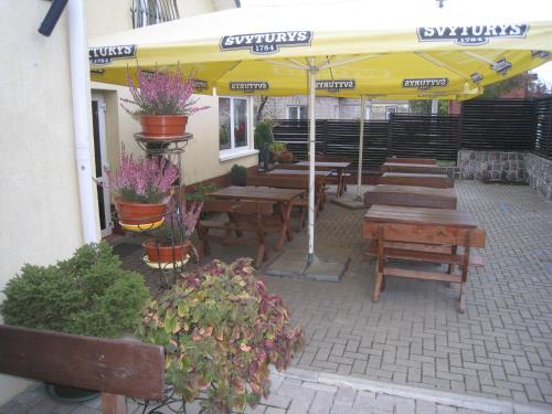 a patio with wooden tables and a yellow umbrella at Aroma Skuodiškio Užeiga in Skuodas