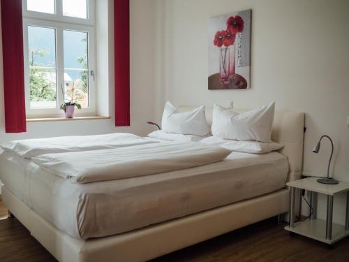 Una cama con sábanas blancas y un jarrón de flores rojas en Hotel Garni Ammergauer Hof, en Oberammergau