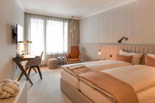 a bedroom with a large bed with a desk and a chair at Kongress Hotel Davos in Davos