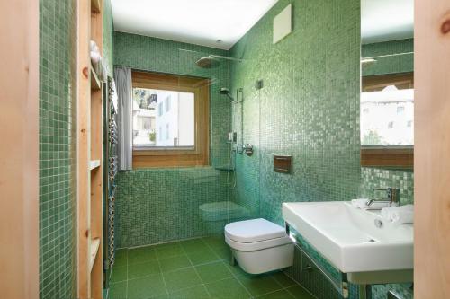 a green bathroom with a toilet and a sink at Alpine Lodge Chesa Plattner in Pontresina